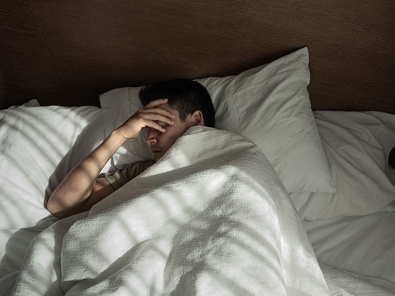 Anxiety,-Depression,-or-Bothr-1 A man is lying in bed and holding his head with his hand