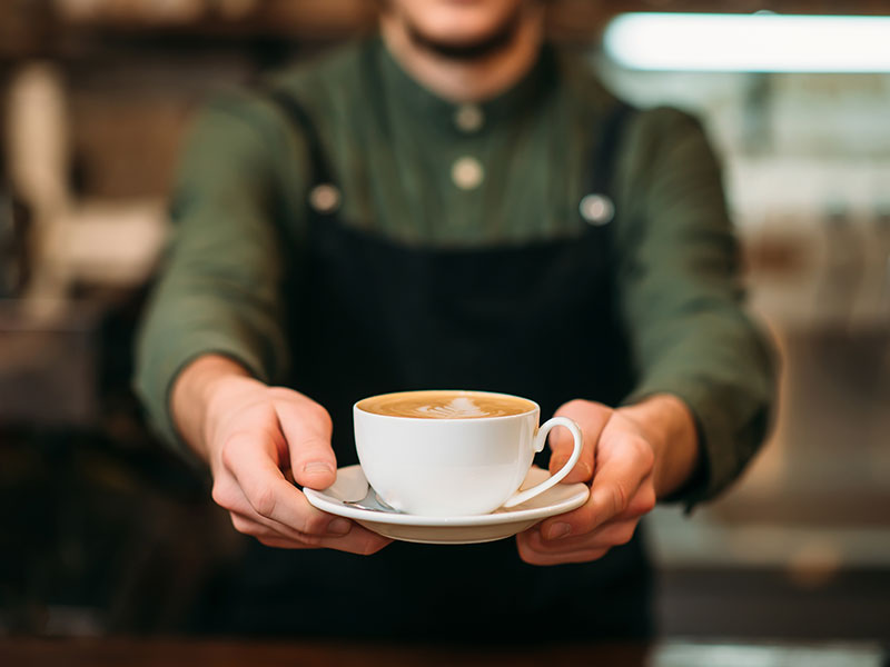 Mental-Health-and-Recovery-Friendly-Coffee-Shops-&-Spaces-in-Philadelphia-Suburbs-1 The barista holds out a cappuccino cup.
