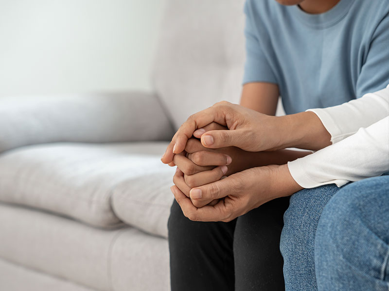 Two people are sitting on a couch and holding hands