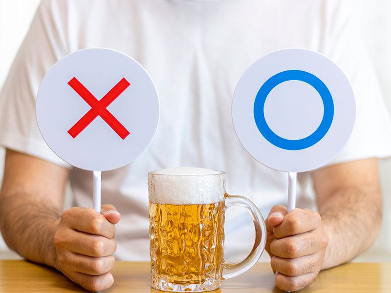 A man holds tic-tac-toe signs in his hands, choosing whether to drink alcohol or not.