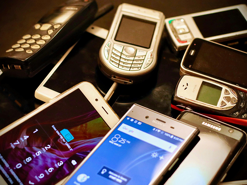 There are many different phones, modern and old, lying on the table.