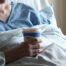 A man is lying in a hospital bed with a glass of coffee